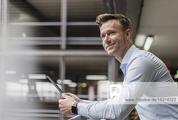 Smiling businessman with digital tablet looking away in city