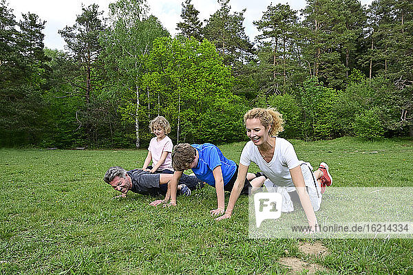 Family doing push-ups on grassy land against trees in forest