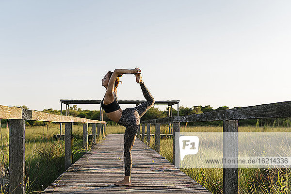 Woman practicing yoga while standing on pier at countryside