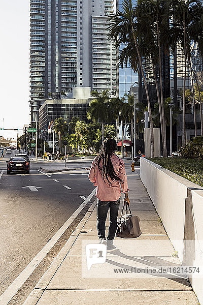 Afro man with dreadlocks holding bag while walking on sidewalk in Miami city  Florida  USA