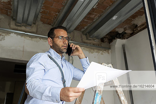 Architect with plan on the phone in a house under construction