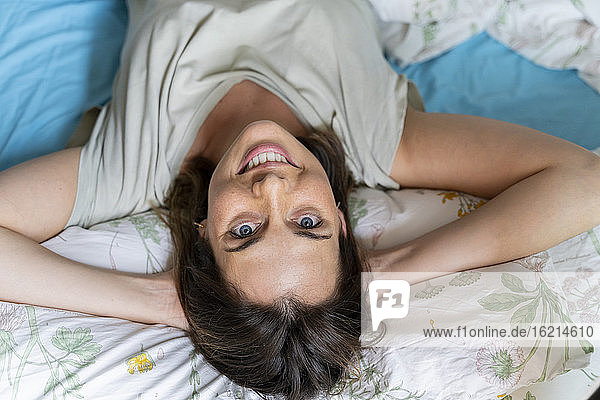 Lächelnde Frau entspannt sich mit den Händen hinter dem Kopf im Schlafzimmer