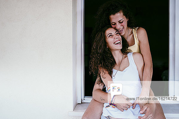 Happy lesbian couple laughing while leaning against window at home