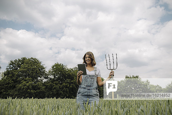 Junge Frau mit Heugabel und Tablette in einem Getreidefeld auf dem Lande