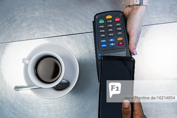 Kunde beim kontaktlosen Bezahlen mit seinem Smartphone in einem Café