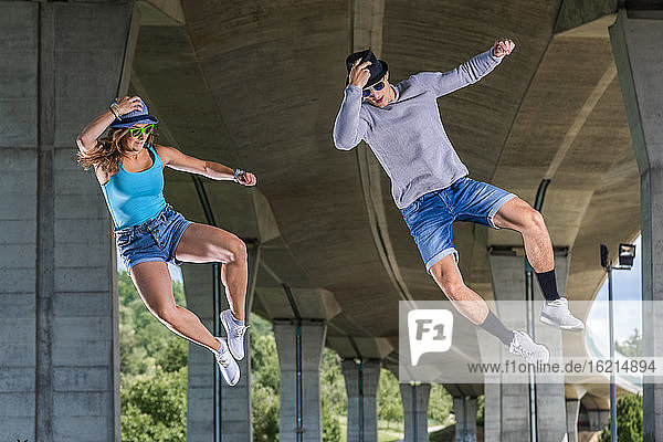 Young couple doing acrobatics under bridge