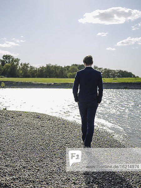 Businessman walking on land at riverbank against sky