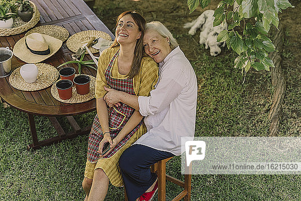 Glückliche Mutter  die ihre Tochter umarmt  während sie am Tisch im Hof sitzt