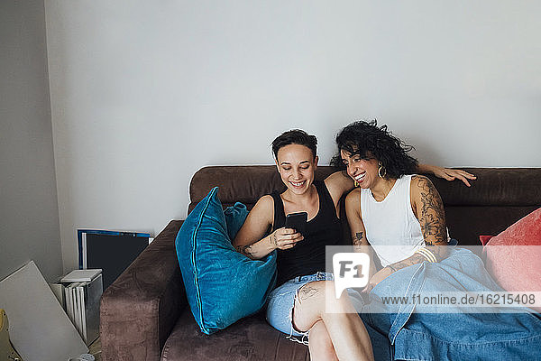 Cheerful couple using phone while sitting on sofa