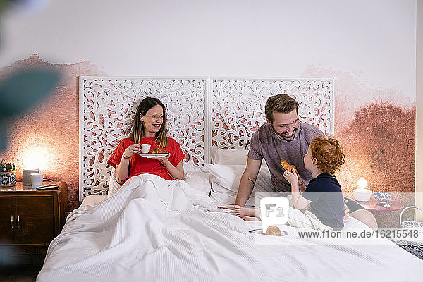 Glückliche Eltern mit Sohn beim Frühstück im Bett zu Hause