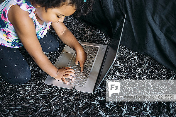 Baby-Mädchen mit Laptop kniend auf Teppich zu Hause