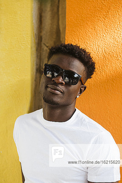 Close-up of young man wearing sunglasses standing against orange wall