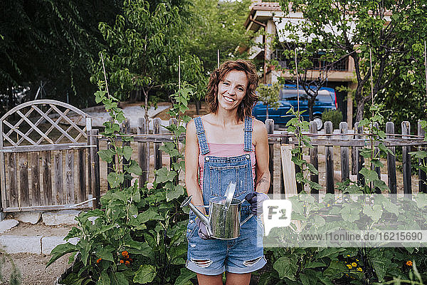 Lächelnde Frau  die eine Gießkanne hält  während sie im Gemüsegarten steht