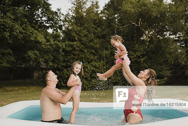 Happy family playing in an inflatable swimming pool in garden