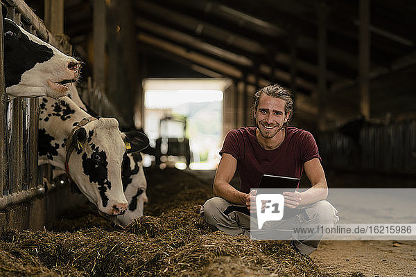Portrait of a smiling young farmer with tablet at cow house on a farm