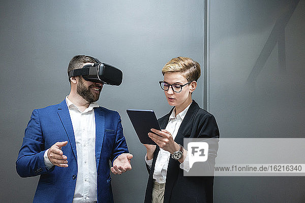 Eine Unternehmerin benutzt ein digitales Tablet  während sie einen Kollegen analysiert  der eine Virtual-Reality-Simulation im Büro erlebt
