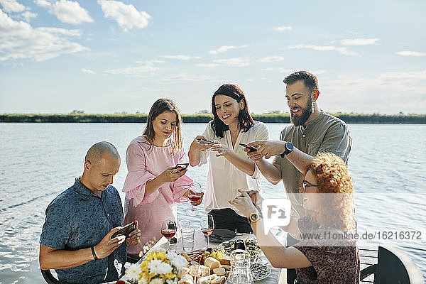 Freunde beim Abendessen am See  die mit dem Smartphone fotografieren
