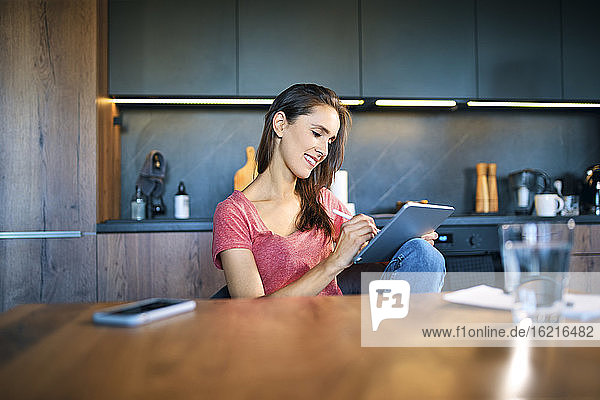 Lächelnde Unternehmerin  die ein digitales Tablet benutzt  während sie am Schreibtisch im Heimbüro sitzt