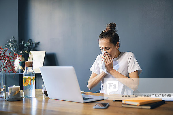 Geschäftsfrau schnäuzt sich die Nase  während sie im Büro zu Hause am Schreibtisch sitzt