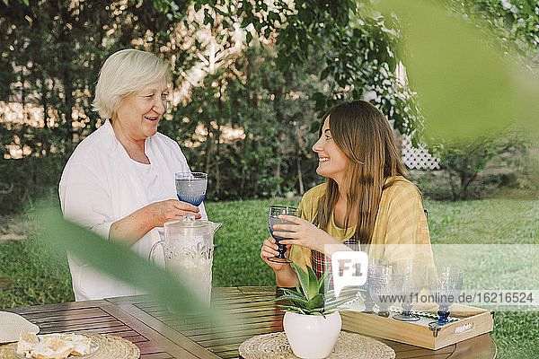 Lächelnde Mutter und Tochter  die im Garten Getränke genießen und sich unterhalten