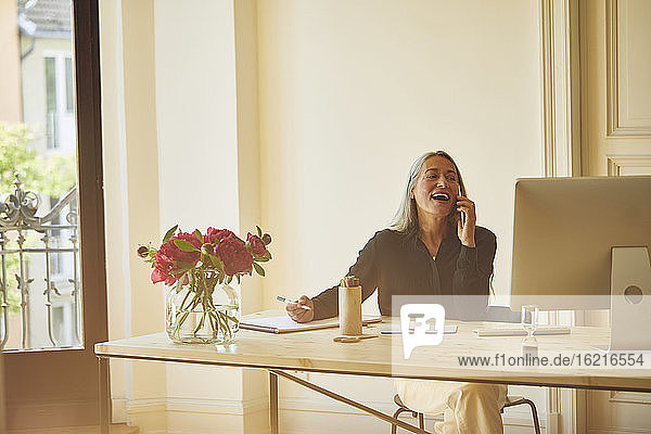 Mature businesswoman talking on phone while working at home