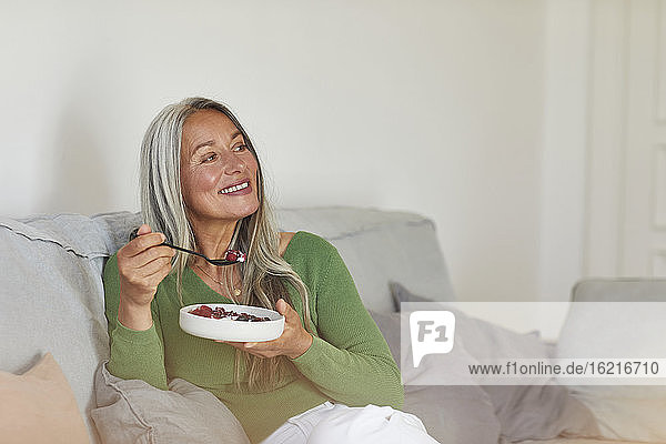 Lächelnde Frau beim Frühstück auf dem Sofa zu Hause