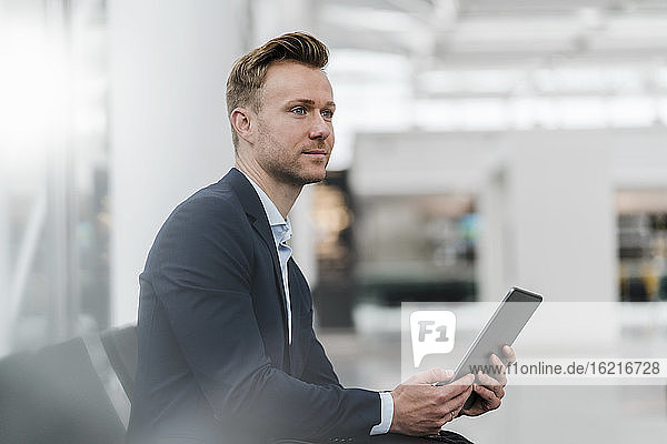 Confident businessman with digital tablet sitting in city