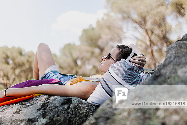 Junge Frau mit Sonnenbrille und Regenbogenflagge auf einem Felsen liegend