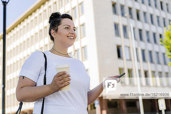 Lächelnde kurvige junge Frau mit Handy in der Stadt