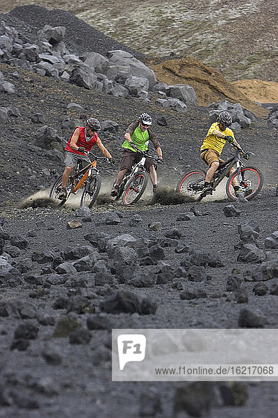 Island  Drei Männer beim Mountainbiking in hügeliger Landschaft