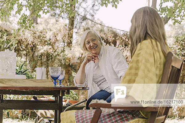 Glückliche ältere Frau im Gespräch mit ihrer Tochter  während sie am Tisch im Hof sitzt