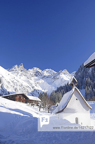 Deutschland  Bayern  Blick auf kleine Kapelle in Dorf mit schneebedeckten Bergen im Hintergrund