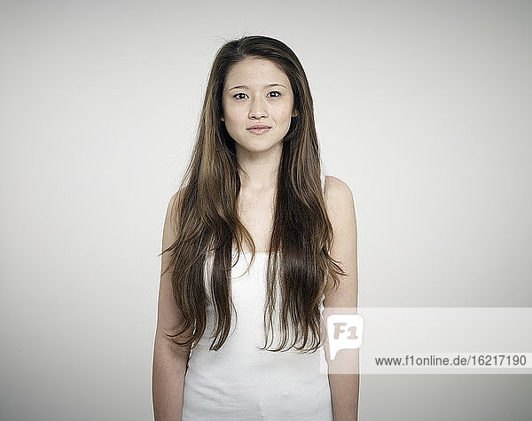 Portrait of young woman standing against white background  smiling