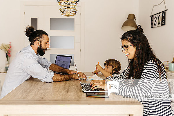 Woman working over laptop while father and daughter painting on dining table at home