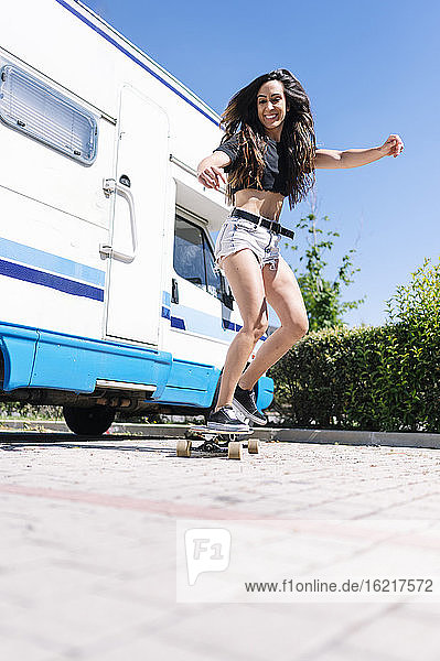 Young woman skateboarding in front of camper