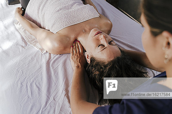 Therapeutin massiert den Nacken einer Kundin  die sich auf einem Tisch im Spa entspannt