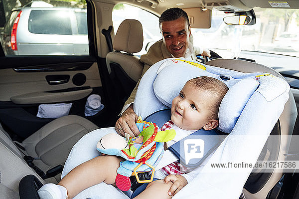 Vater befestigt Baby im Kindersitz im Auto