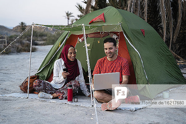 Young woman wearing Hijab and man using laptop at a tent