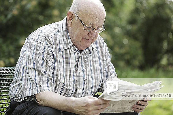 Deutschland  Nordrhein-Westfalen  Köln  Älterer Mann  der auf einer Bank im Park Zeitung liest