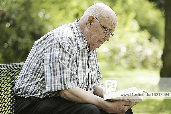 Deutschland  Nordrhein-Westfalen  Köln  Älterer Mann liest Buch auf Bank im Park