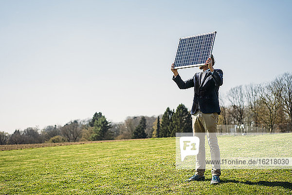 Male professional holding solar panel while standing on grass at park against clear sky during sunny day
