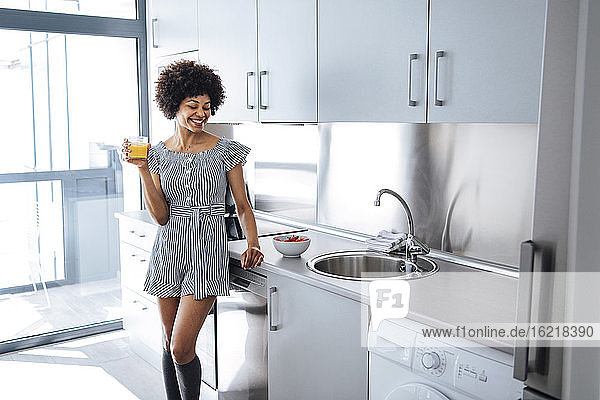 Glückliche Frau hält ein Glas Orangensaft in einer modernen Küche in einem Penthouse