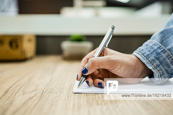 Geschäftsfrau Hand schreiben auf Dokument auf hölzernen Schreibtisch in modernen Büro