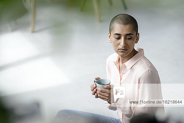 Porträt einer ernsten Frau  die in einem Loft auf dem Boden sitzt und eine Tasse Kaffee hält