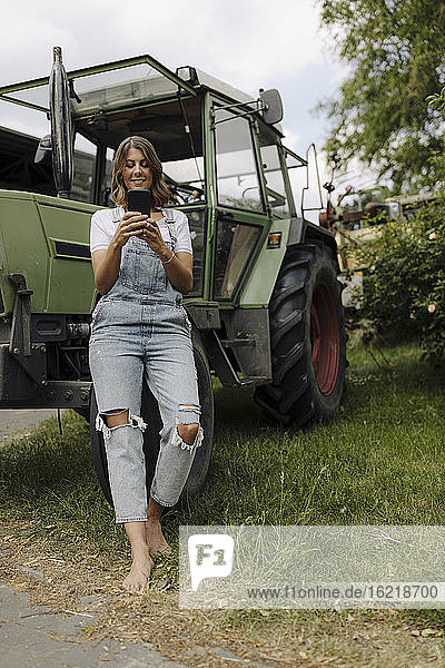 Junge Frau benutzt ein Mobiltelefon an einem Traktor auf dem Lande