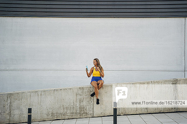 Blond athletic woman taking a selfie  sitting on wall