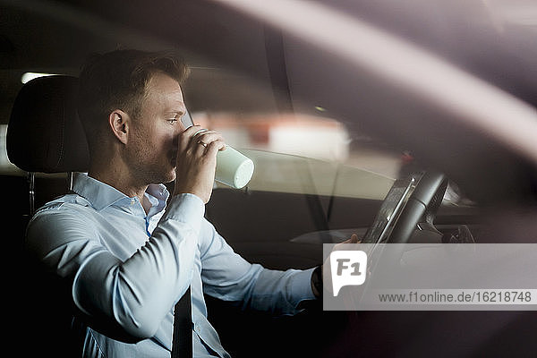 Businessman drinking coffee while reading online on digital tablet in car