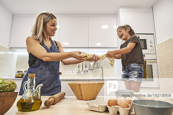 Fröhliche Mutter und Tochter kneten Pizzateig in der Küche zu Hause