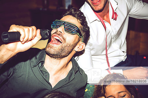Nahaufnahme eines jungen Mannes  der Karaoke singt und sich mit Freunden auf einer Party amüsiert