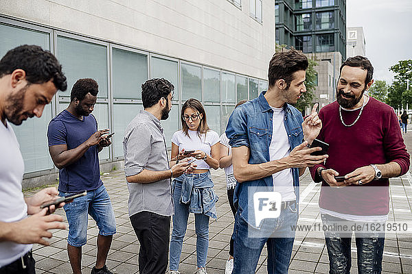 Freunde unterhalten sich und benutzen Smartphones  während sie auf einem Fußweg in der Stadt stehen